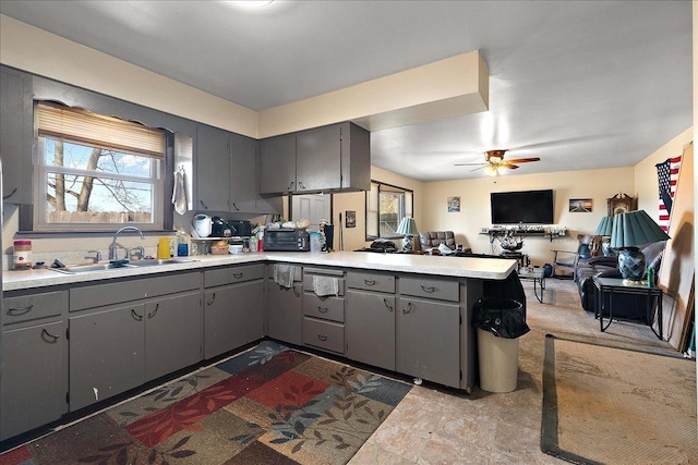 kitchen featuring open floor plan, light countertops, gray cabinets, a peninsula, and a sink