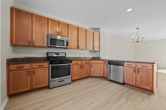 kitchen featuring a peninsula, light wood-style flooring, dark stone counters, a sink, and appliances with stainless steel finishes