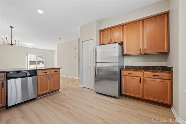 kitchen with dark stone countertops, brown cabinets, appliances with stainless steel finishes, and light wood finished floors