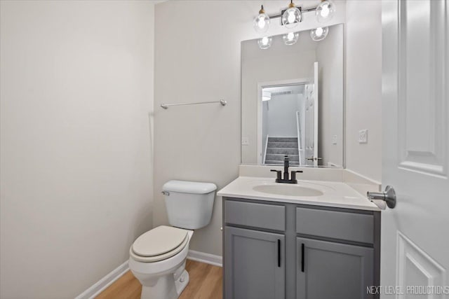 bathroom with toilet, vanity, baseboards, and wood finished floors