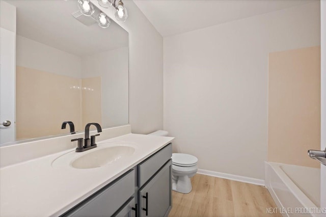 bathroom with vanity, wood finished floors, baseboards, a tub to relax in, and toilet