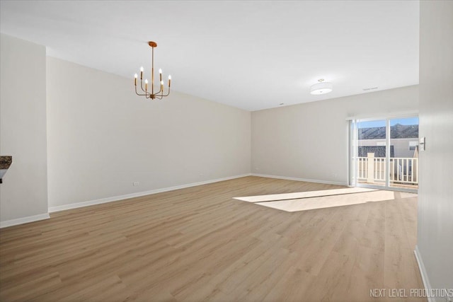 empty room with a notable chandelier, baseboards, and wood finished floors