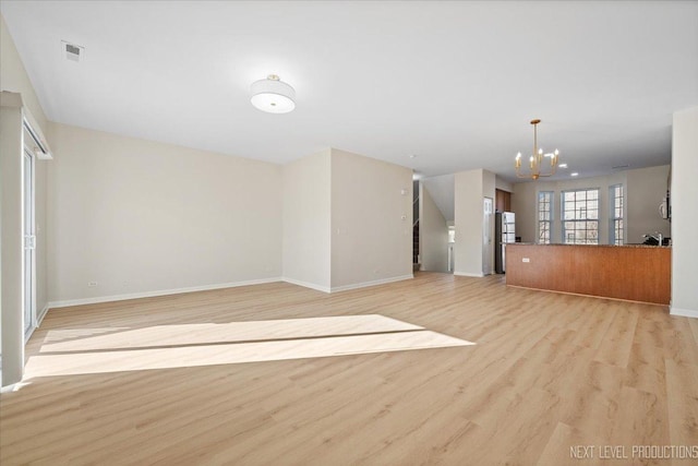 unfurnished living room with light wood finished floors, a chandelier, visible vents, and baseboards