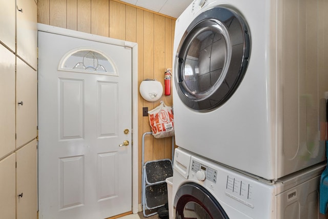 clothes washing area with laundry area, stacked washer / dryer, and wooden walls