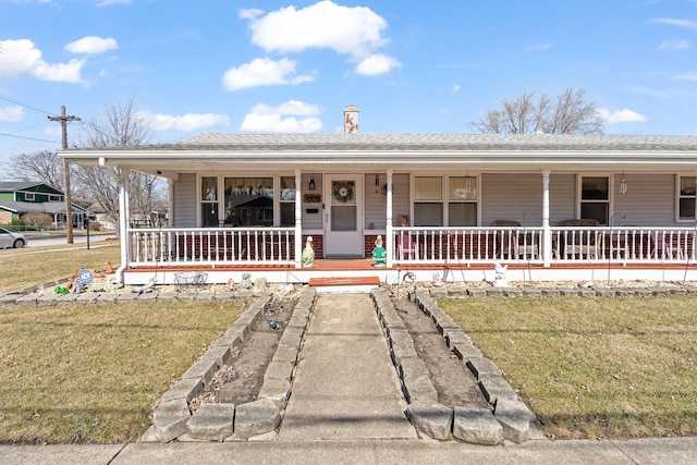 view of front facade with a front yard, covered porch, and roof with shingles