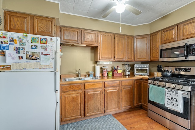 kitchen with a sink, light wood-style floors, appliances with stainless steel finishes, brown cabinetry, and light countertops