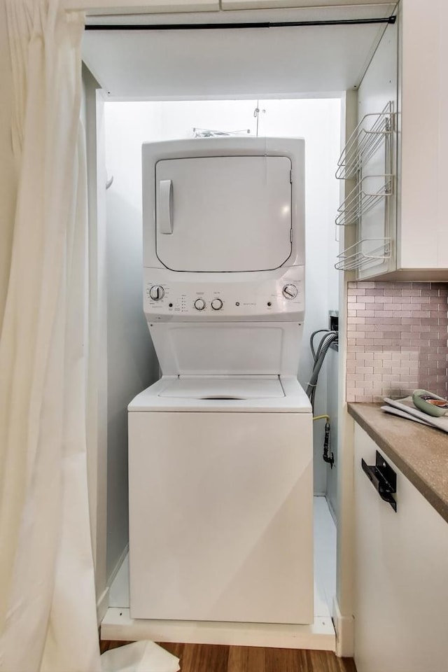 clothes washing area with laundry area, stacked washer and dryer, and wood finished floors