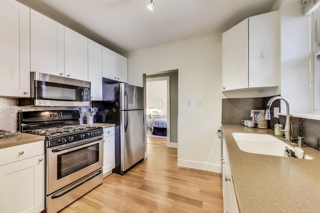 kitchen featuring a sink, tasteful backsplash, appliances with stainless steel finishes, white cabinets, and light wood finished floors