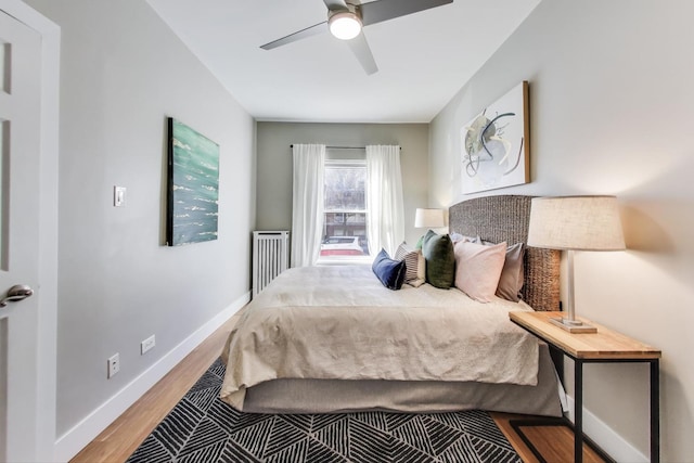 bedroom with a ceiling fan, radiator, wood finished floors, and baseboards