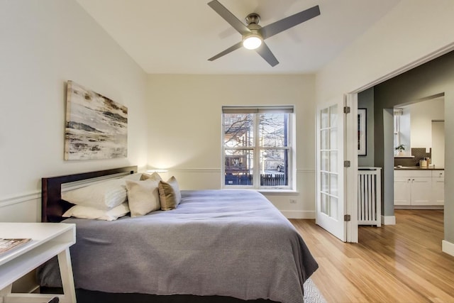 bedroom with light wood finished floors, baseboards, radiator heating unit, ensuite bath, and a ceiling fan