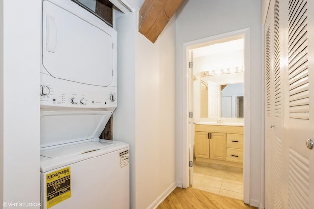 clothes washing area with stacked washer / drying machine, a sink, laundry area, baseboards, and light wood-style floors