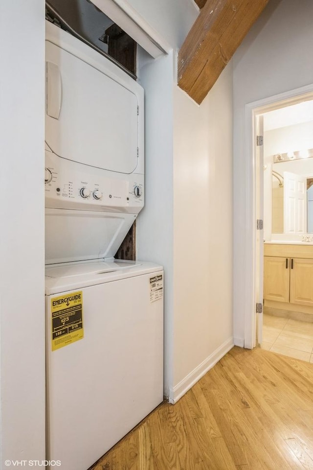 washroom featuring laundry area, stacked washer / drying machine, baseboards, and light wood-style floors