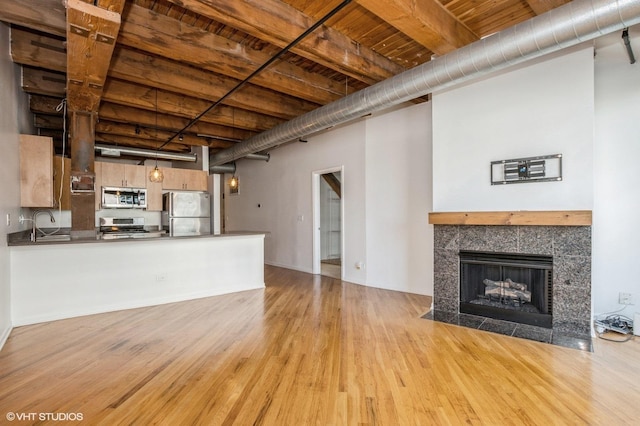 unfurnished living room featuring light wood-style flooring, a sink, wood ceiling, beamed ceiling, and a fireplace