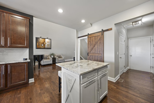 kitchen featuring dark wood-style floors, backsplash, a barn door, and light stone counters