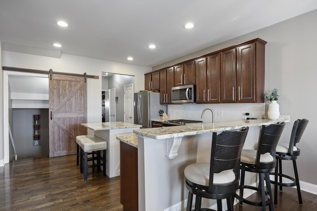 kitchen featuring a peninsula, decorative backsplash, appliances with stainless steel finishes, a barn door, and a kitchen breakfast bar