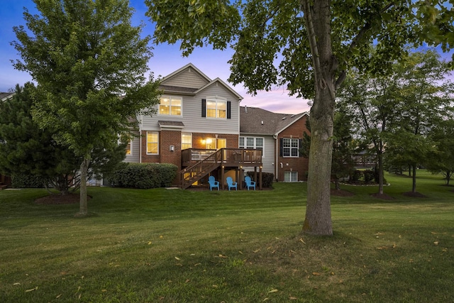 back of property at dusk featuring brick siding, stairway, a lawn, and a wooden deck