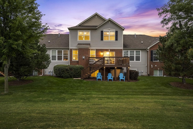 back of property at dusk featuring stairs, a wooden deck, brick siding, and a lawn