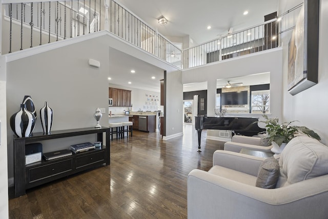 living room with dark wood-type flooring, baseboards, ceiling fan, recessed lighting, and a high ceiling