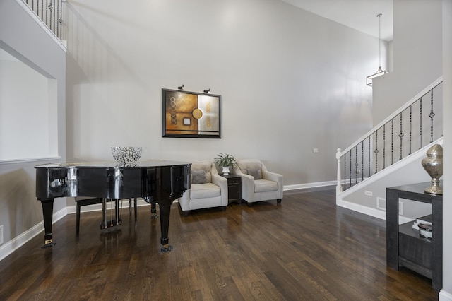 living area with stairway, wood finished floors, baseboards, and a towering ceiling