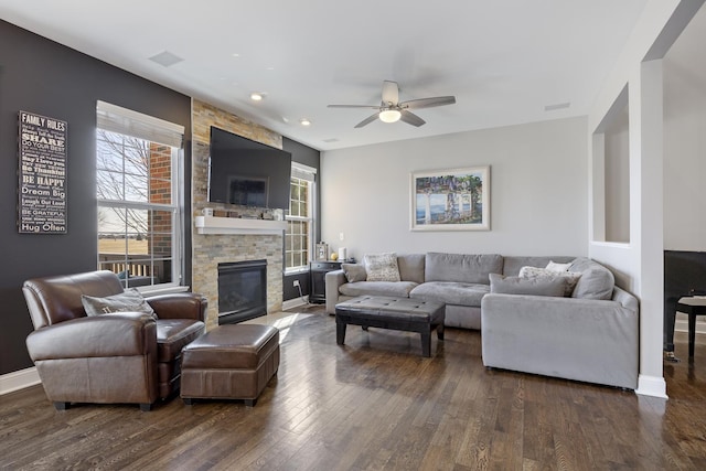 living room featuring visible vents, baseboards, a stone fireplace, dark wood-style floors, and a ceiling fan