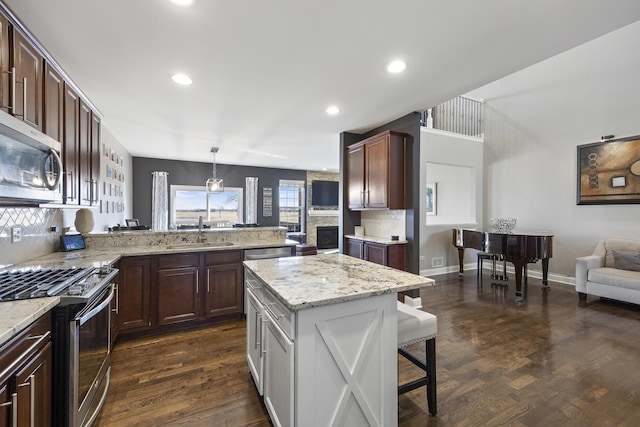 kitchen with a peninsula, dark wood-style flooring, a sink, stainless steel appliances, and a kitchen breakfast bar