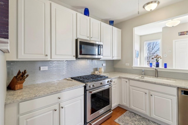 kitchen featuring tasteful backsplash, white cabinetry, stainless steel appliances, and a sink