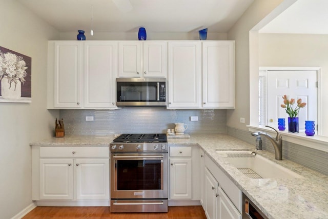 kitchen with tasteful backsplash, white cabinets, appliances with stainless steel finishes, and a sink