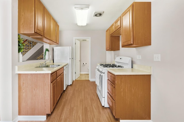 kitchen with baseboards, light countertops, light wood-style flooring, white appliances, and a sink