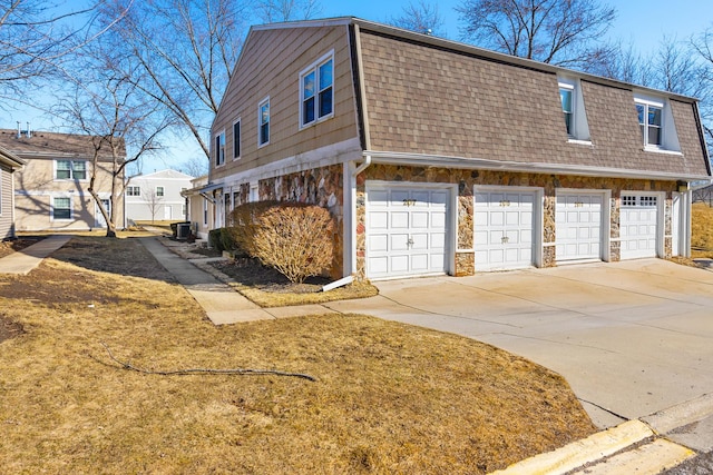 view of home's exterior featuring stone siding, central AC, roof with shingles, concrete driveway, and an attached garage