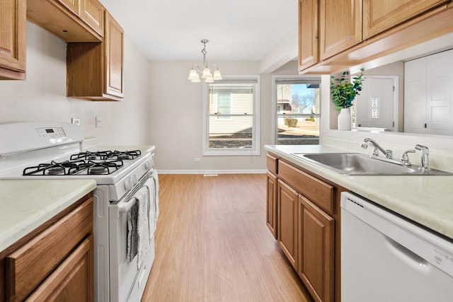 kitchen featuring white appliances, light wood-style flooring, a sink, light countertops, and a notable chandelier