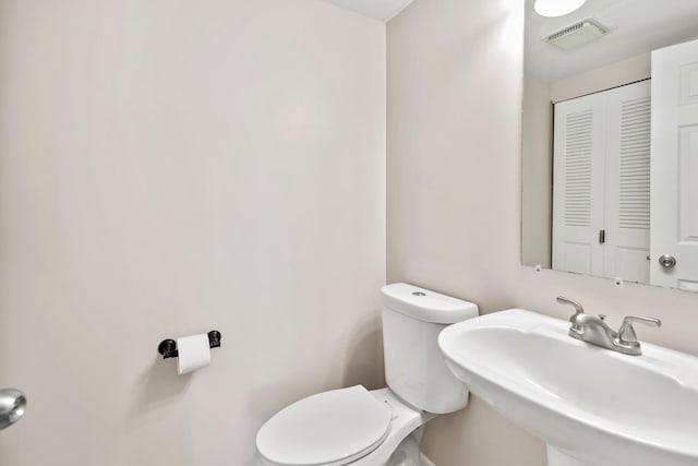 half bath with visible vents, toilet, and a sink