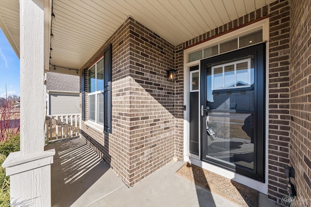 view of exterior entry with brick siding and a porch