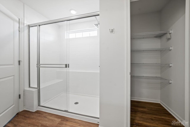 bathroom with a spacious closet, wood finished floors, and a stall shower