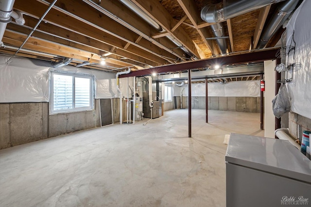 basement featuring gas water heater, heating unit, a healthy amount of sunlight, and freestanding refrigerator