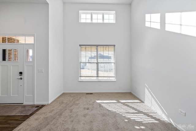 foyer entrance featuring baseboards, a towering ceiling, and carpet flooring