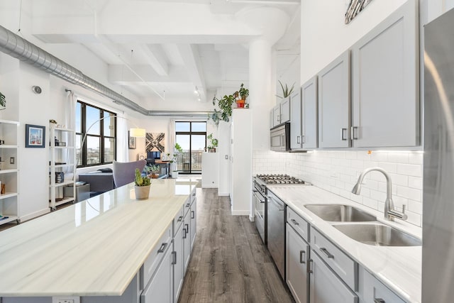 kitchen with a kitchen island, dark wood finished floors, a sink, appliances with stainless steel finishes, and beamed ceiling