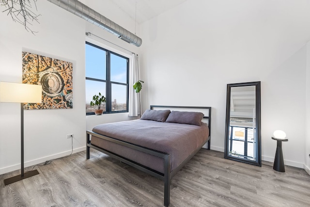 bedroom featuring a towering ceiling, baseboards, and wood finished floors