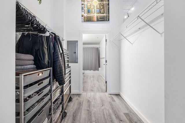 walk in closet featuring electric panel, wood finished floors, and a towering ceiling