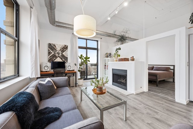 living area with a high ceiling, a fireplace with raised hearth, light wood-style flooring, and track lighting