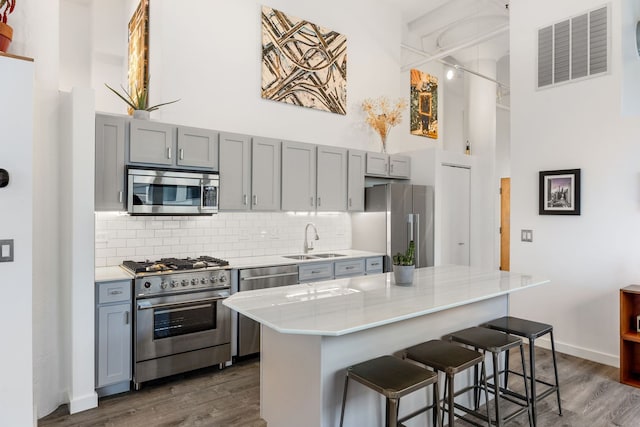 kitchen with visible vents, gray cabinets, a sink, appliances with stainless steel finishes, and a towering ceiling