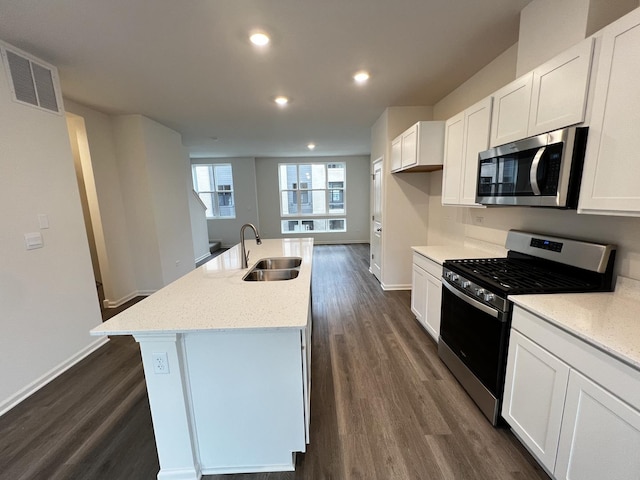 kitchen with a kitchen island with sink, dark wood finished floors, appliances with stainless steel finishes, white cabinetry, and a sink