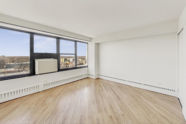 empty room featuring a baseboard radiator, a city view, wood finished floors, and a baseboard heating unit