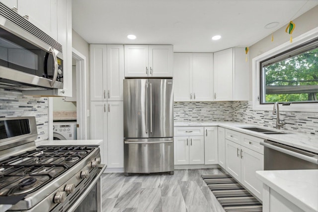 kitchen featuring light stone countertops, a sink, stainless steel appliances, white cabinetry, and backsplash