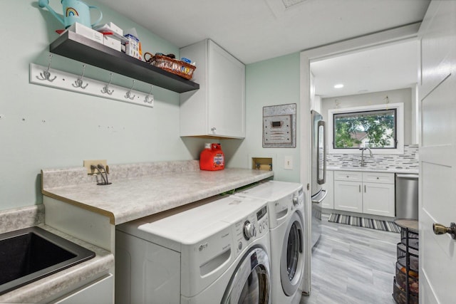 laundry area with cabinet space, washing machine and dryer, light wood finished floors, and a sink