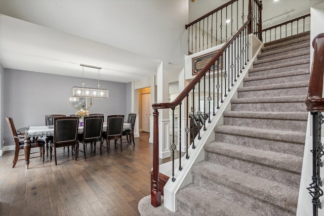 stairs featuring baseboards, wood-type flooring, a notable chandelier, and a towering ceiling