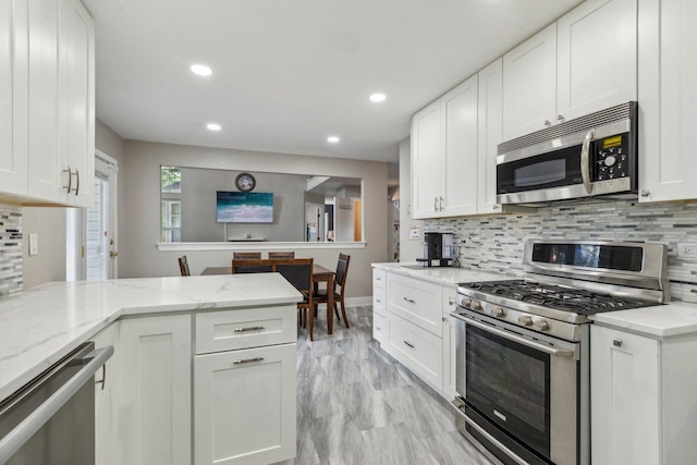 kitchen with light stone counters, stainless steel appliances, tasteful backsplash, and white cabinetry