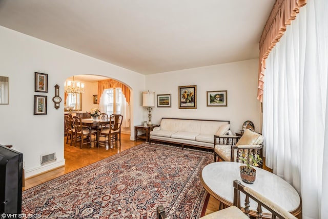 living room with visible vents, wood finished floors, arched walkways, baseboards, and a chandelier