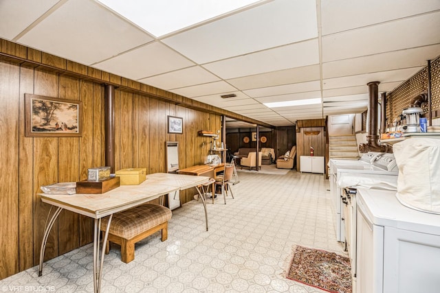 dining space with wooden walls, a drop ceiling, washing machine and dryer, light floors, and stairs