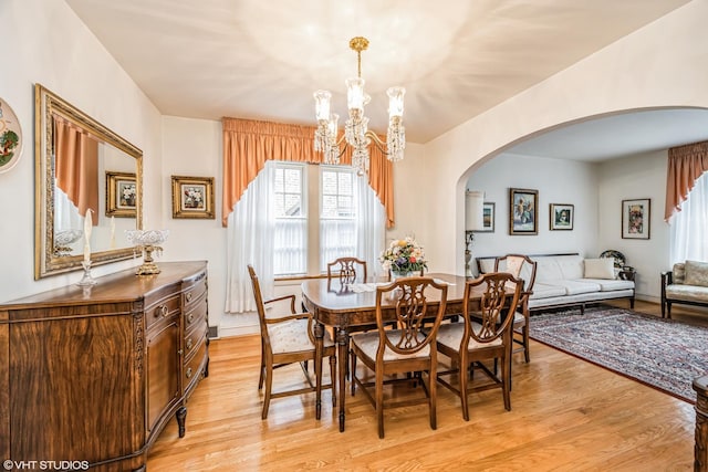 dining area with arched walkways, a notable chandelier, and light wood-style flooring