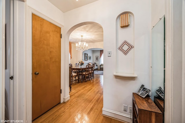 hall with baseboards, arched walkways, a notable chandelier, and light wood finished floors